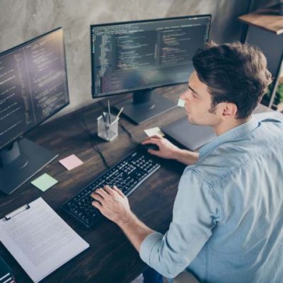 man on computer with multiple monitors, appears to be coding in multiple windows with dual monitors
