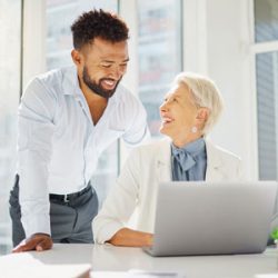 Young business person helps older business person with computer
